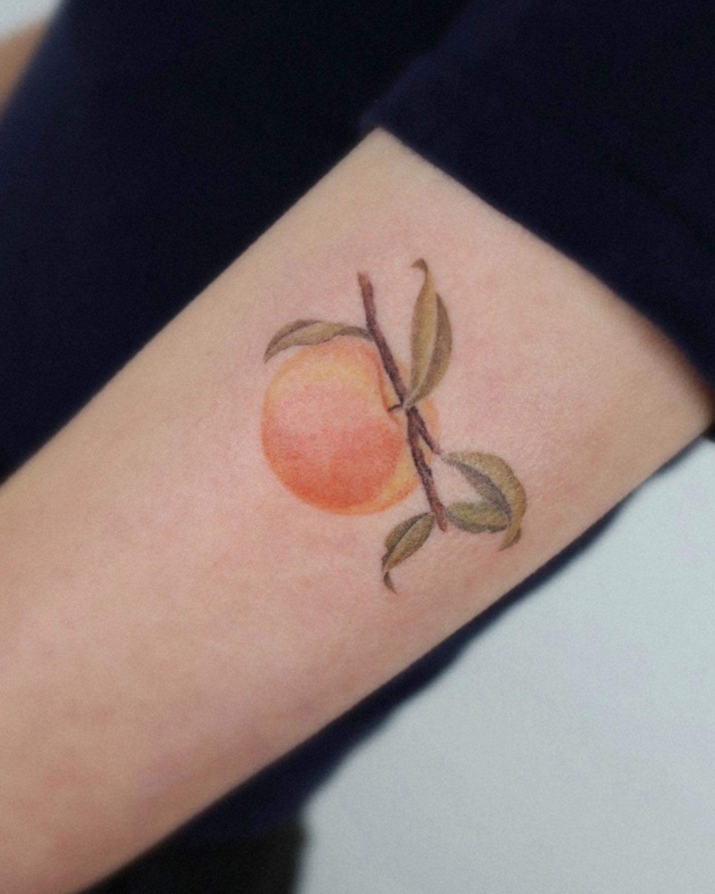 A vibrant peach tattoo with leaves on a forearm